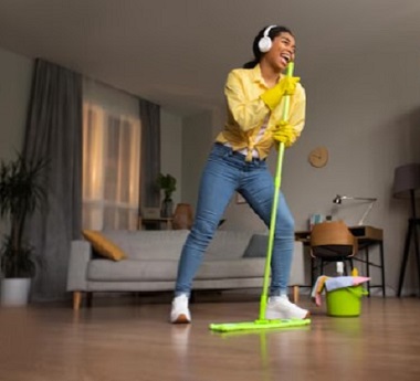 A young lady singing and listening to music while mopping the floor.